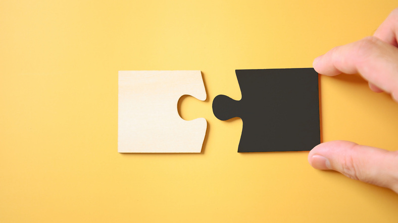 Hand holding the jigsaw puzzle pieces white and color black together on yellow background